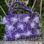 Handtasche aus violettem Stoff mit fliederfarbener Borte und fliederfarbenen Puscheln. Innenfutter fliederfarben. 218.- €